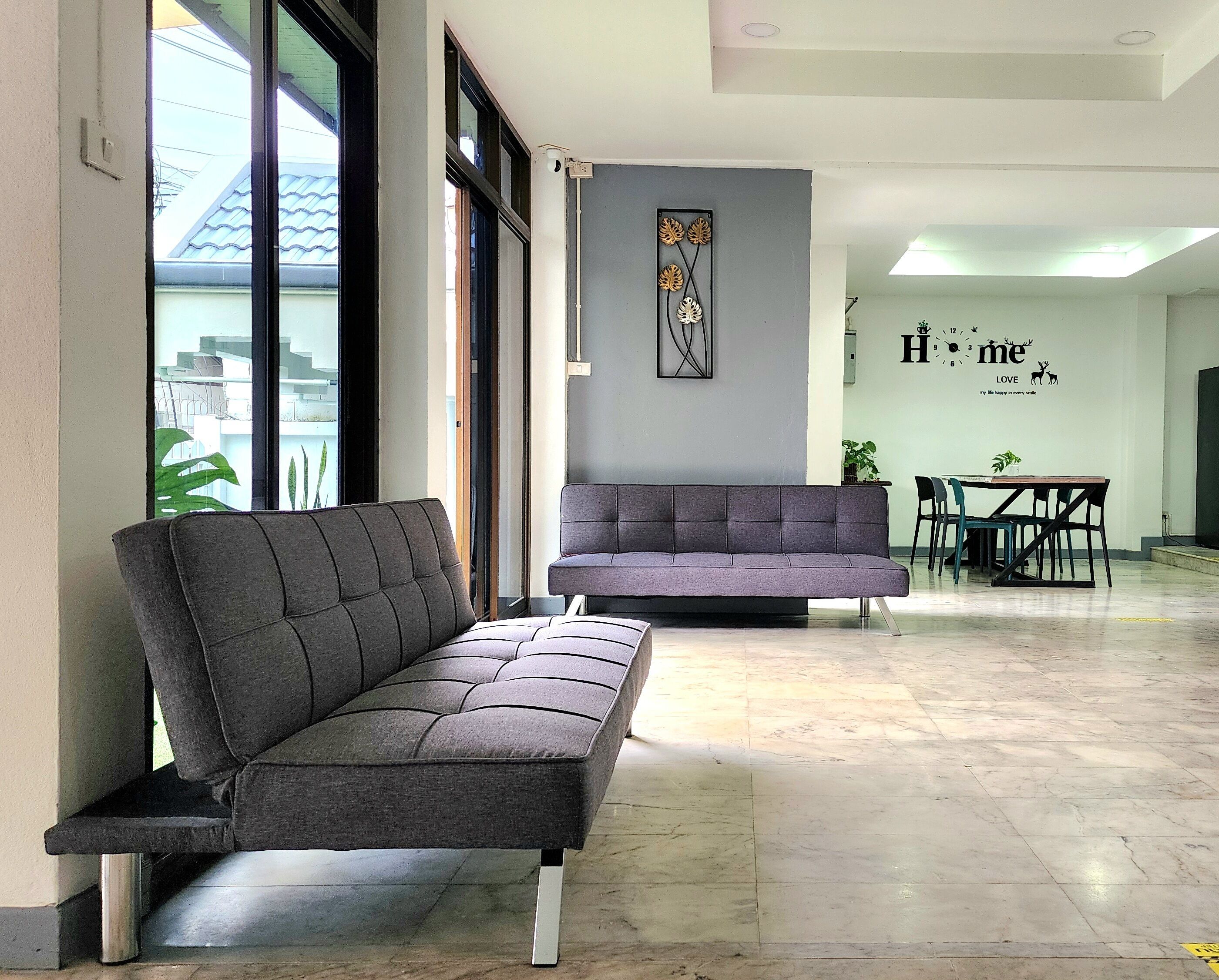 A modern interior with two grey sofas, a dining area with a table and chairs, and a wall with a clock and decorative elements.