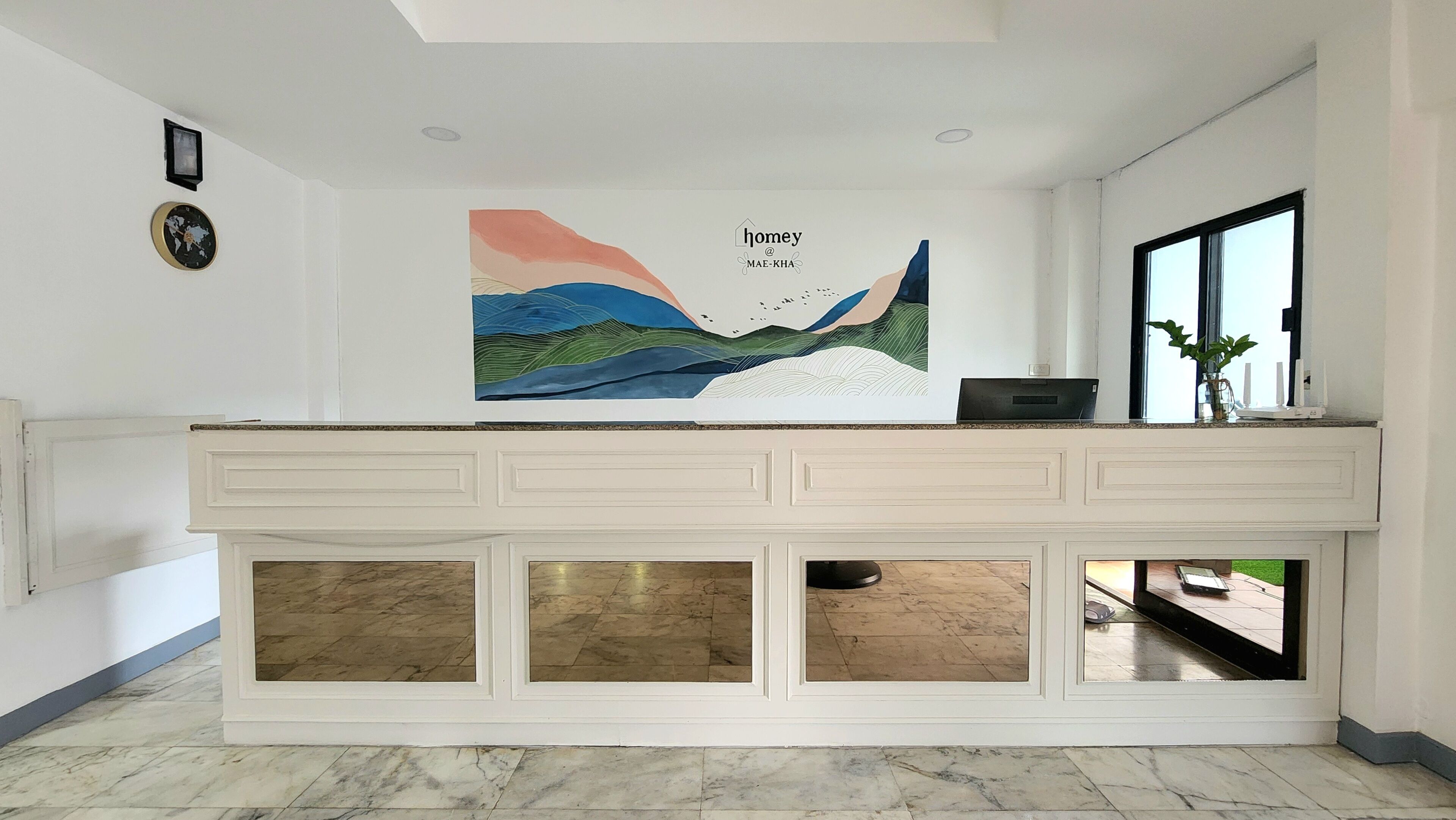 A modern reception desk with a large abstract painting above it, a world clock, and a window with a view.