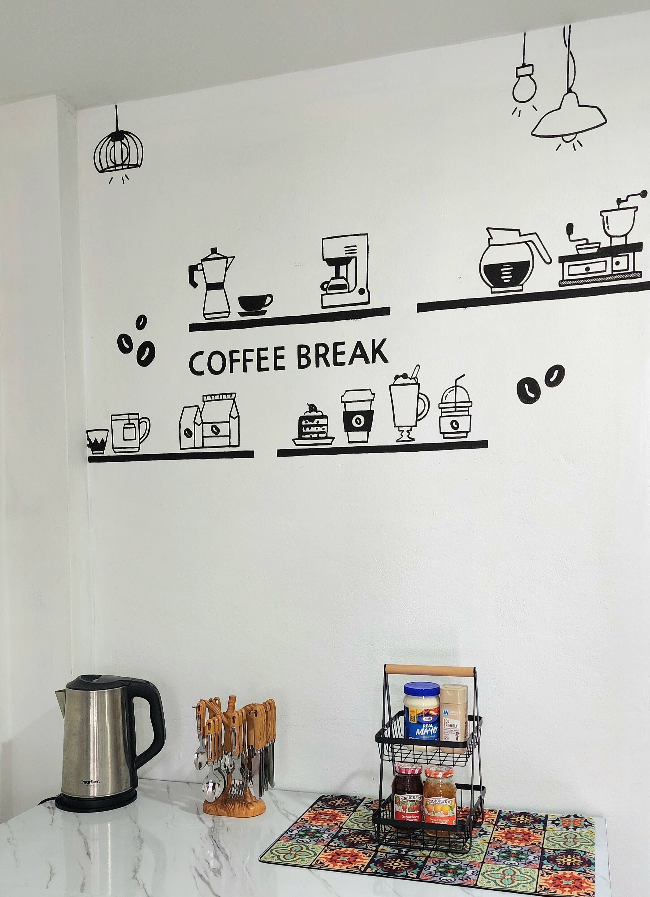 Una pared de cocina con un cartel de pausa para café, una cafetera, un hervidor y un estante con especias.