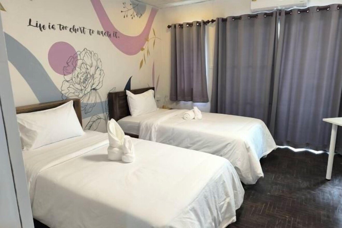 A hotel room with two beds, a wall mural, and grey curtains.