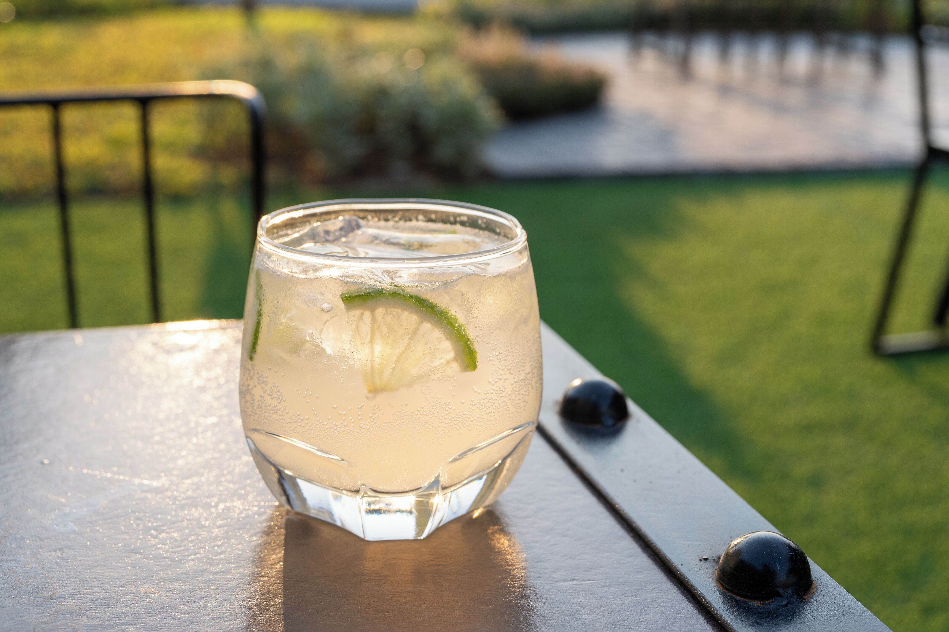 A glass of iced beverage with a lime wedge on a metal table outdoors.