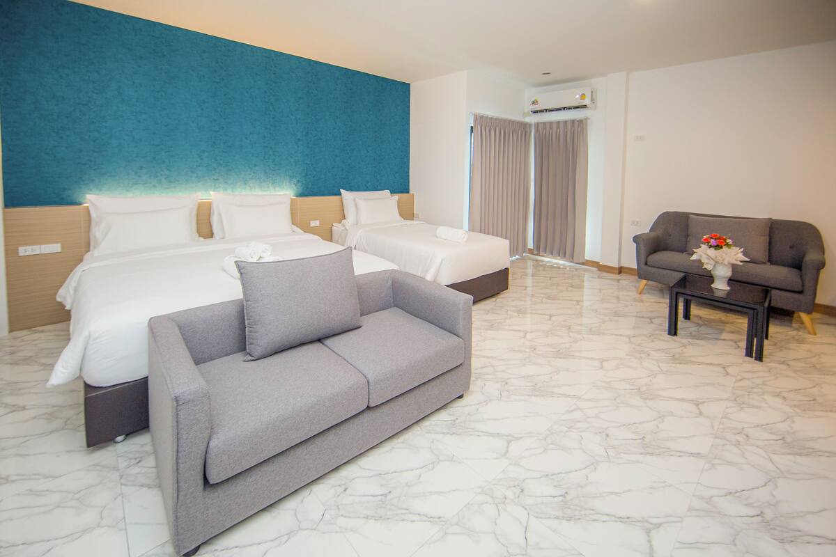 Ein Hotelzimmer mit zwei Betten, einem grauen Sofa, einem Couchtisch und einer Blumenvase.
