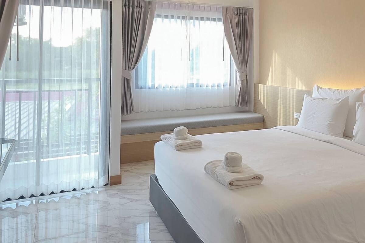 Ein Hotelzimmer mit einem großen Bett, einem Fenster mit Vorhängen und Blick ins Freie.