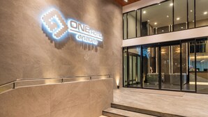 Een moderne hotelentree met een opvallend verlicht bord, een glazen deur en een trap naar de lobby.