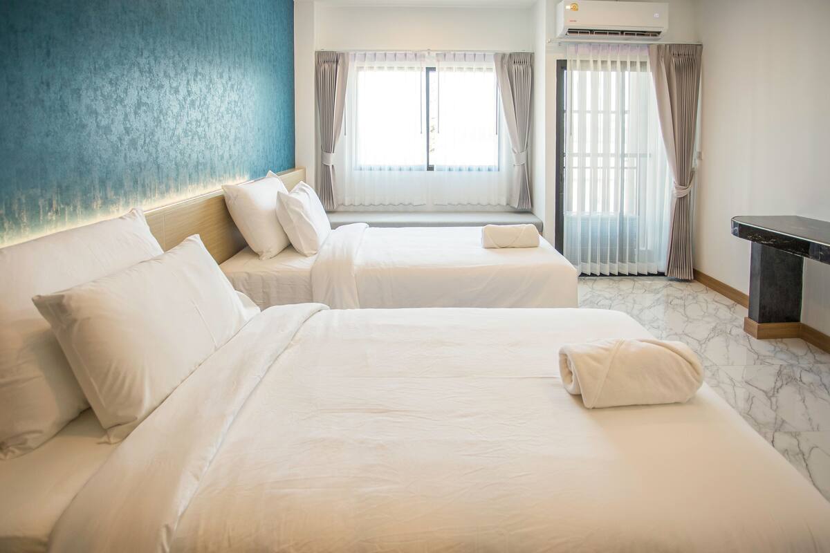 Ein Hotelzimmer mit zwei Betten, einem großen Fenster mit Vorhängen, einer Klimaanlage und einem Marmorboden.