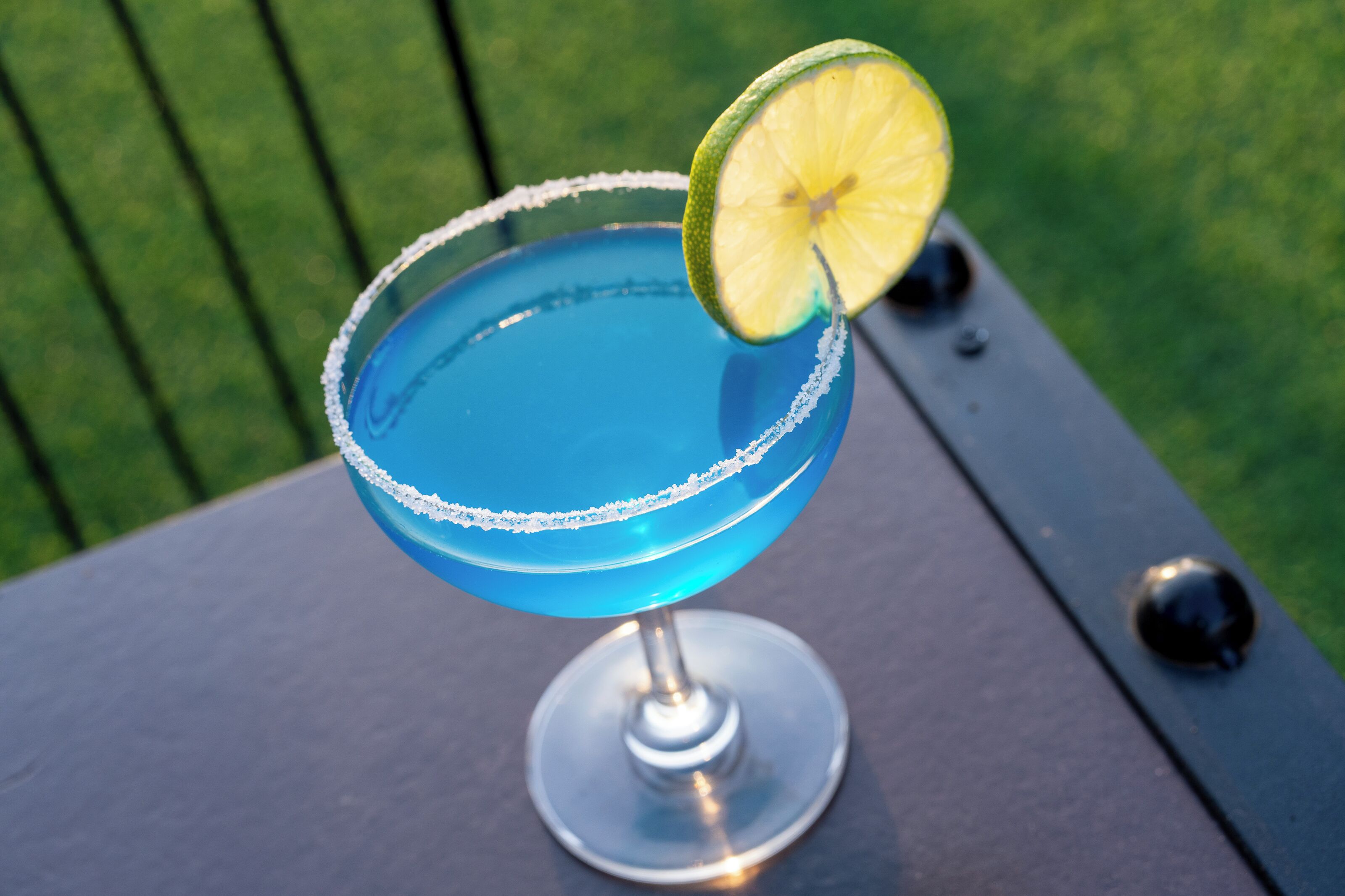 Un cocktail bleu, garni d’une tranche de citron vert, servi dans un verre dont le bord est saupoudré de sel, posé sur une table.