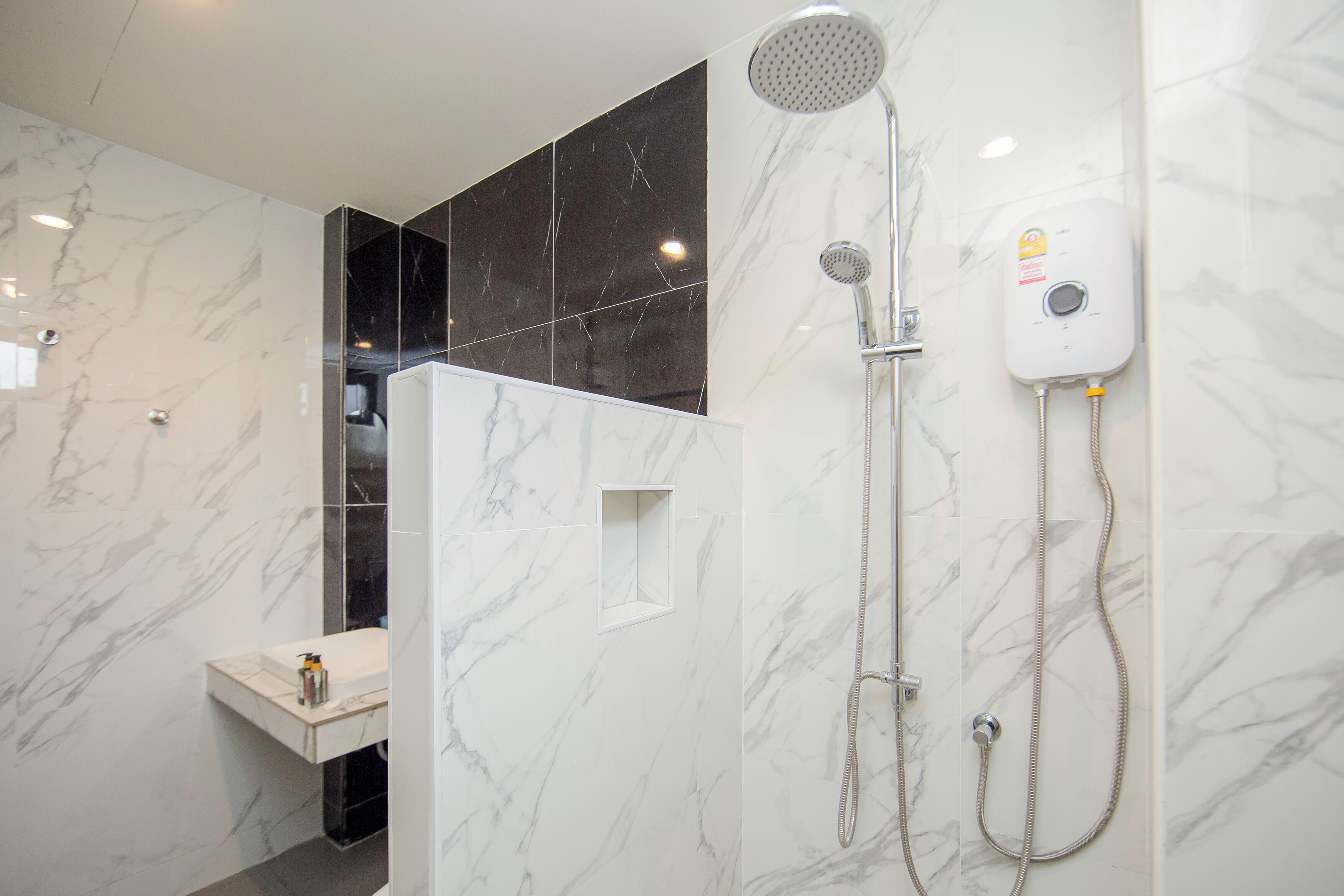 A modern bathroom with a marble shower enclosure, a handheld showerhead, and a wall-mounted control panel.