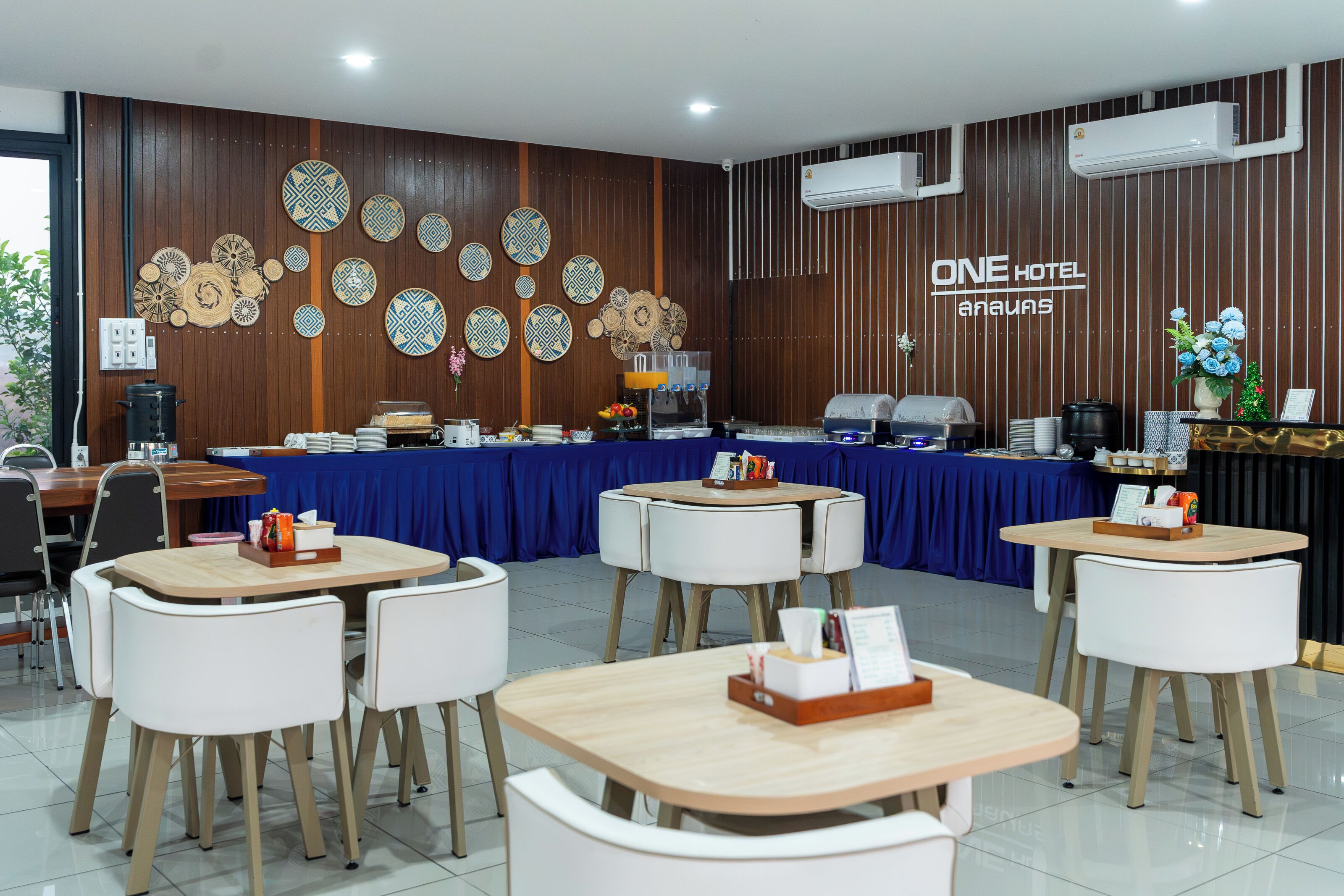 Une salle à manger d’hôtel avec une nappe bleue, des chaises blanches et un mur décoré d’assiettes.