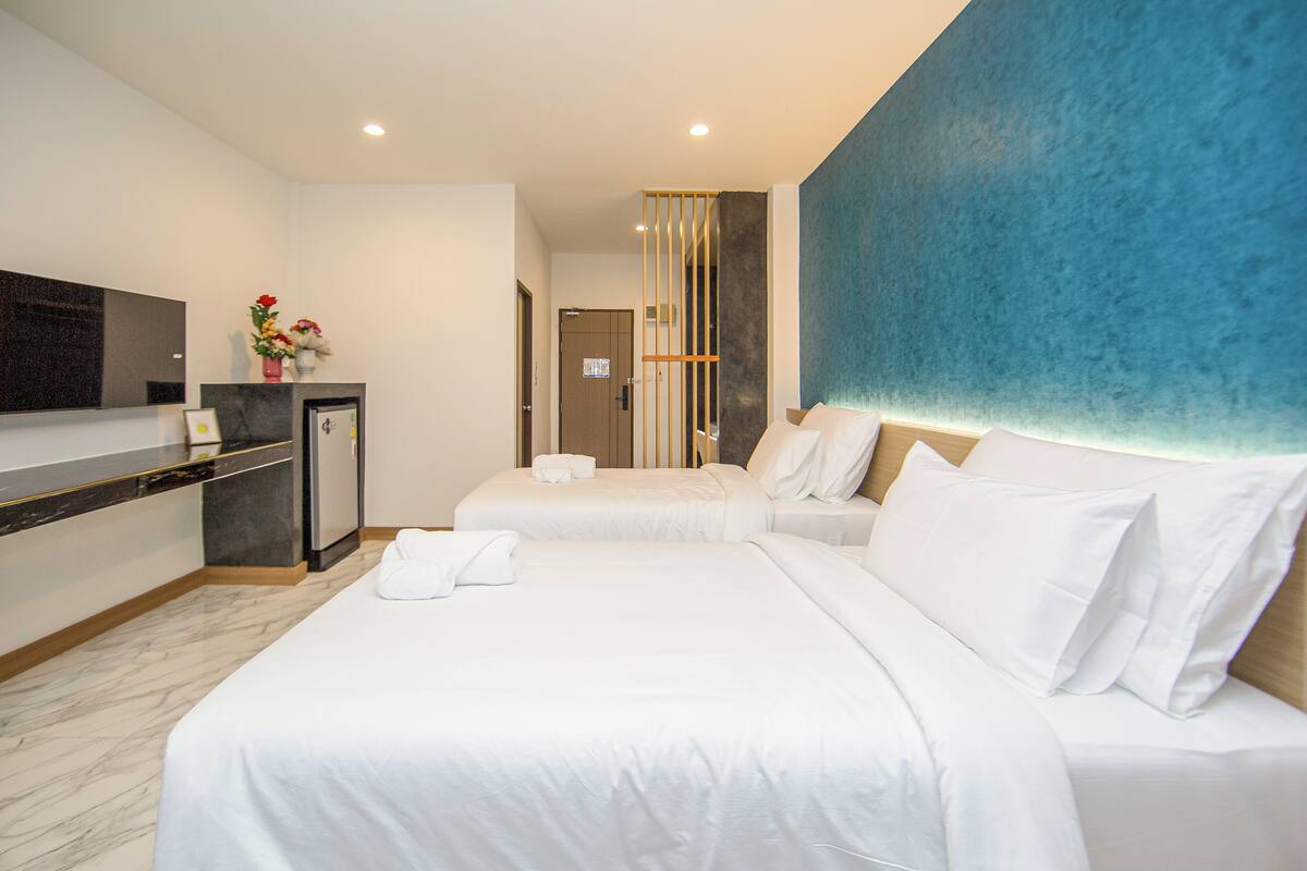 Ein Hotelzimmer mit zwei Betten, einer Minibar, einem Flachbildfernseher und einer blauen Akzentwand.