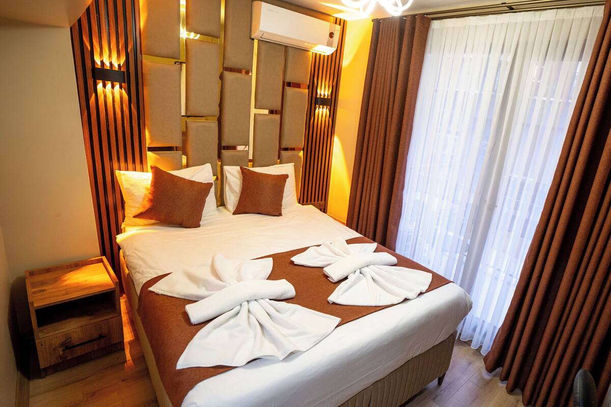 A hotel room with a large bed, brown curtains, and a wooden headboard.