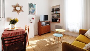 Olohuoneessa on sohva, televisio, kirjahylly, ruokapöytä tuoleineen sekä seinällä aurinkomainen peili.