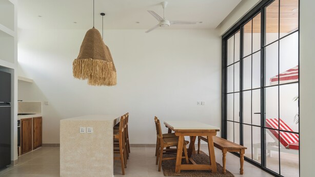 A modern kitchen with wooden cabinets, a central island, and a dining area with a table and chairs. - Villa Mauka by Alfred in Bali (Canggu)