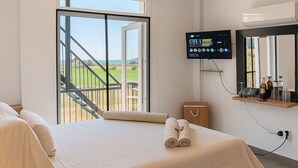 A hotel room with a bed, a TV, a small table with bottles, and a balcony with a view of the sea. - Comfy room with sea view in Villa private pool fitness room in adorable Oroklini (Oroklini)