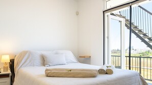 A hotel room with a bed, a nightstand with a lamp, a window with a view of the outside, and a balcony with a staircase. - Comfy room with sea view in Villa private pool fitness room in adorable Oroklini (Oroklini)