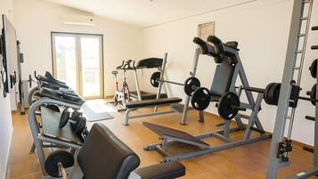 Et fitnesscenter med forskellig træningsudstyr, herunder en bænkpres, et løbebånd og en motionscykel.