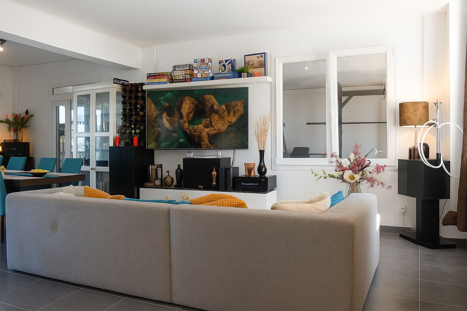 Un salon moderne avec un canapé gris, un téléviseur à écran plat et une bibliothèque contenant des livres et des objets décoratifs.
