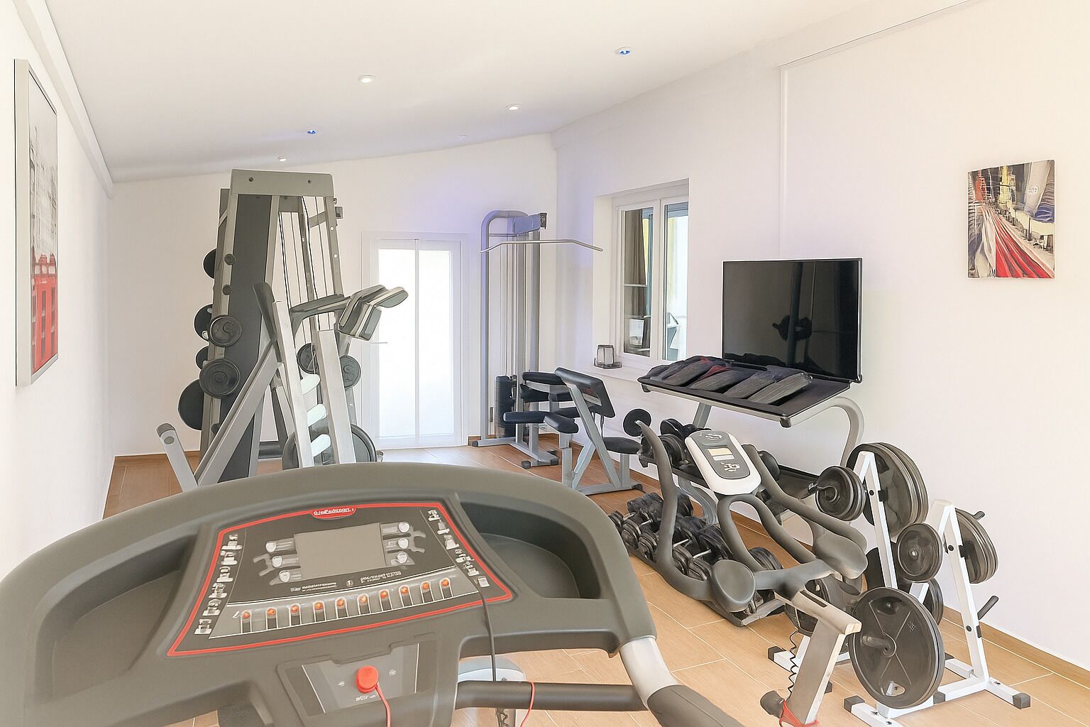 Een fitnessruimte met diverse trainingsapparaten, waaronder een loopband, een hometrainer en gewichtstoestellen.