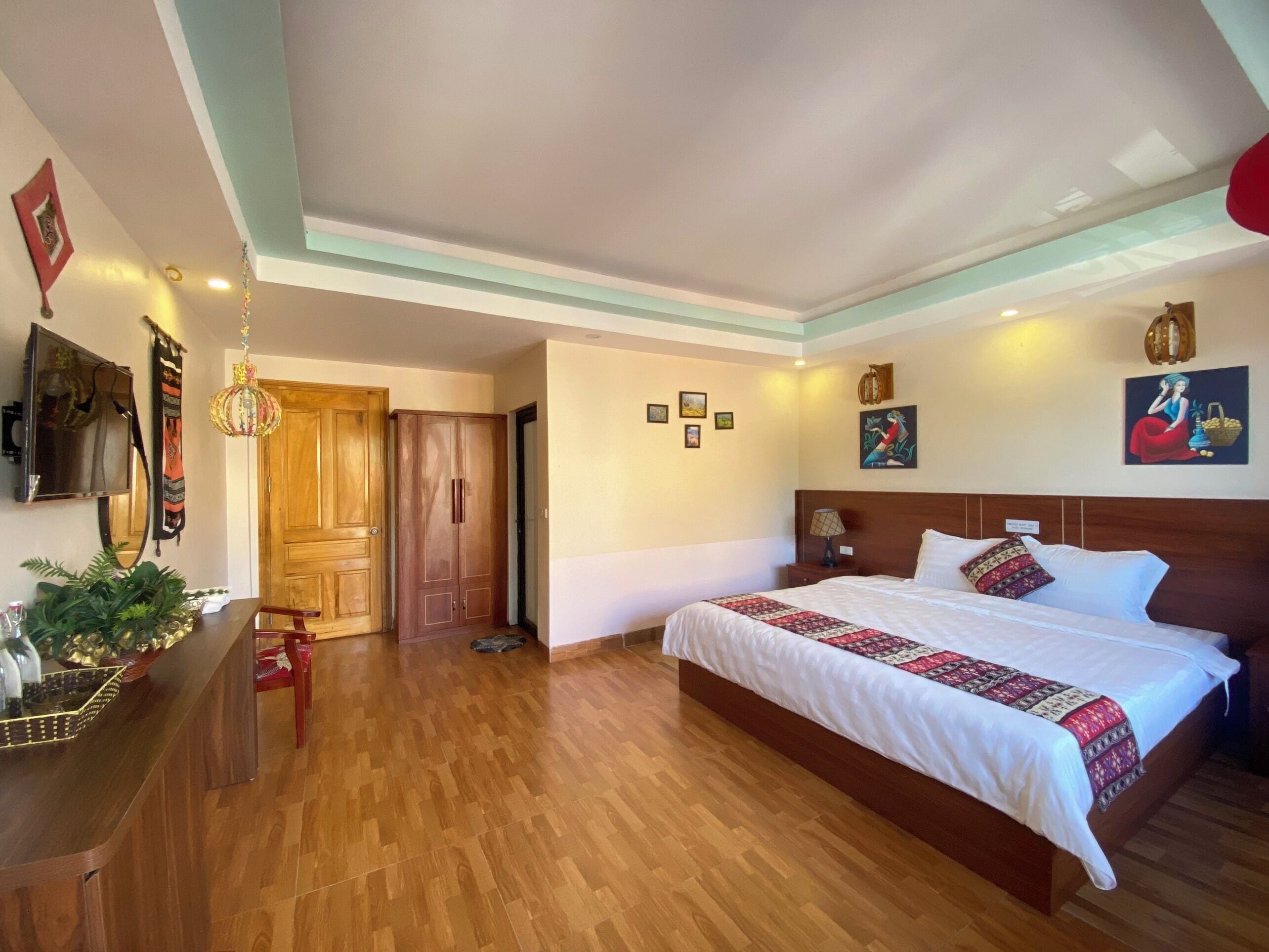 A hotel room with a large bed, wooden flooring, a wooden wardrobe, a TV, and a chandelier.