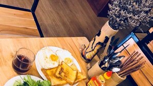 A dining table with plates of food, including fried eggs and toast, a glass of dark liquid, and a bottle of sauce. - Misty Hostel Sapa (Sa Pa)
