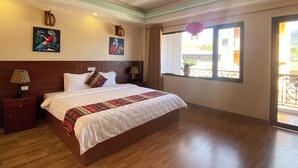 A hotel room with a large bed, wooden flooring, two wall-mounted lamps, a window with a view, and artwork on the walls. - Misty Hostel Sapa (Sa Pa)