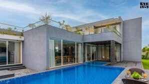 Een modern huis met een zwembad, grote raampartijen en een terras met tuinmeubilair.