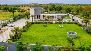 Een modern huis met een groot gazon, een auto op de oprit en uitzicht op het omliggende landschap.