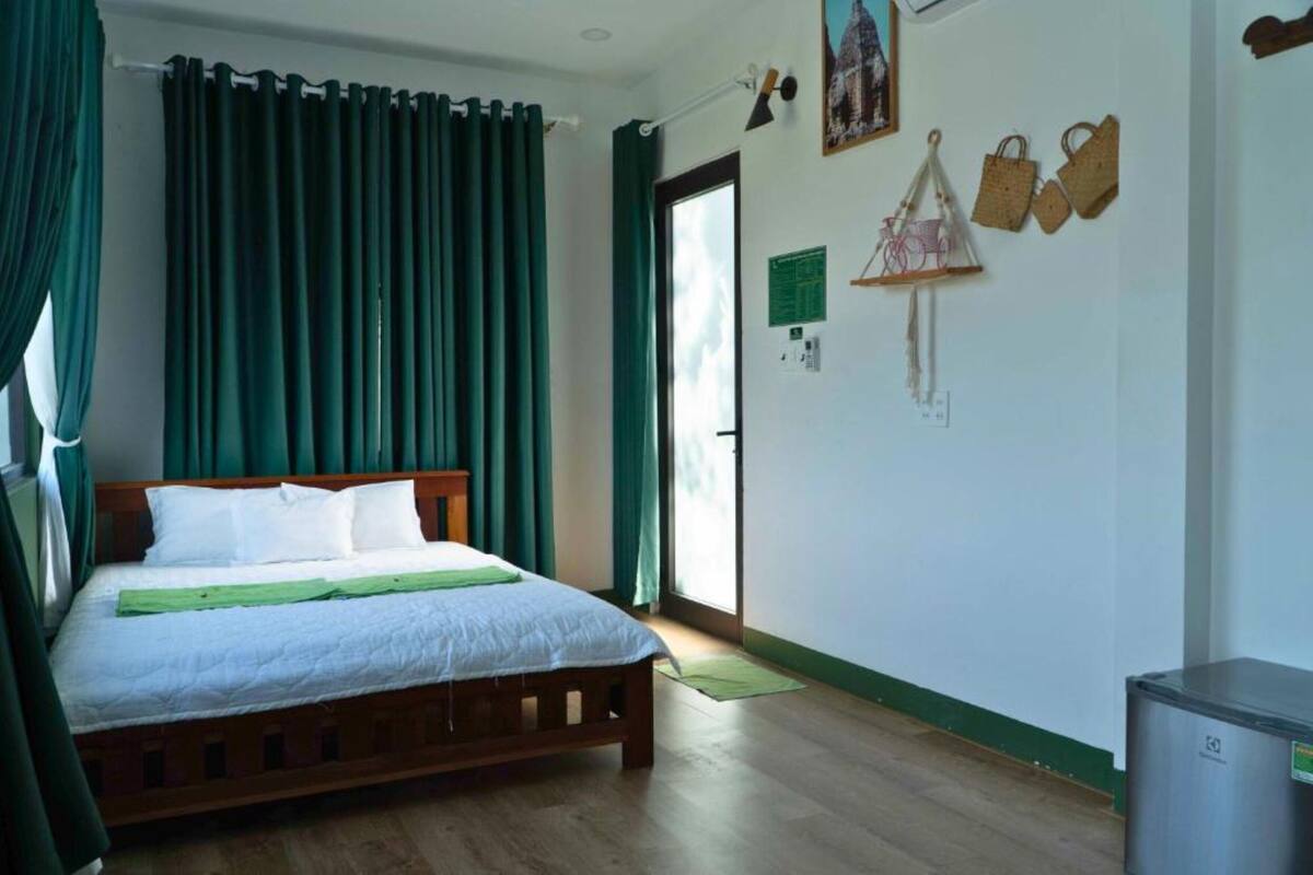 Ein Schlafzimmer mit einem hölzernen Bett, grünen Vorhängen, einer grünen Matte und einem kleinen Kühlschrank.