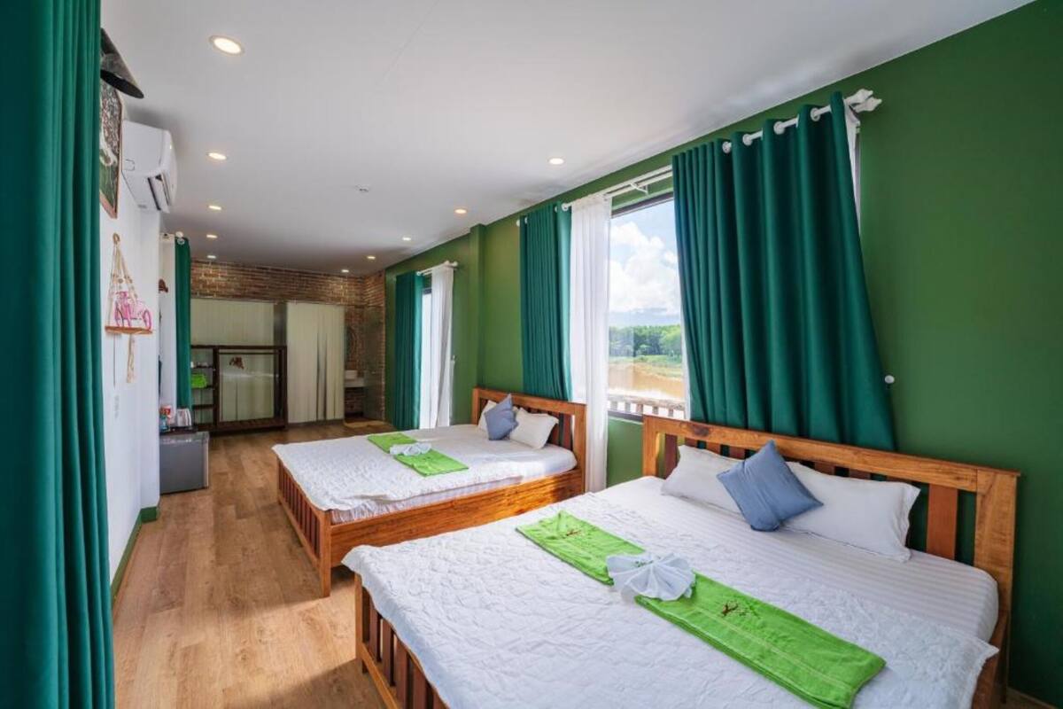 Ein Hotelzimmer mit zwei Betten, grünen Vorhängen und Blick ins Freie.