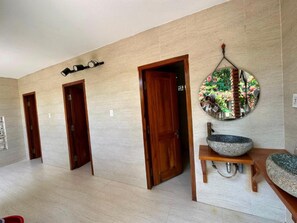 Un pasillo con tres puertas de madera, un espejo redondo sobre un fondo floral y un lavabo de piedra en una mesa de madera.