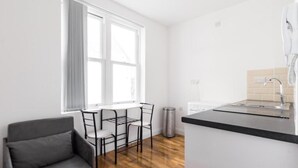 Una cocina moderna con encimera negra, ventana con cortinas blancas y un sofá gris.