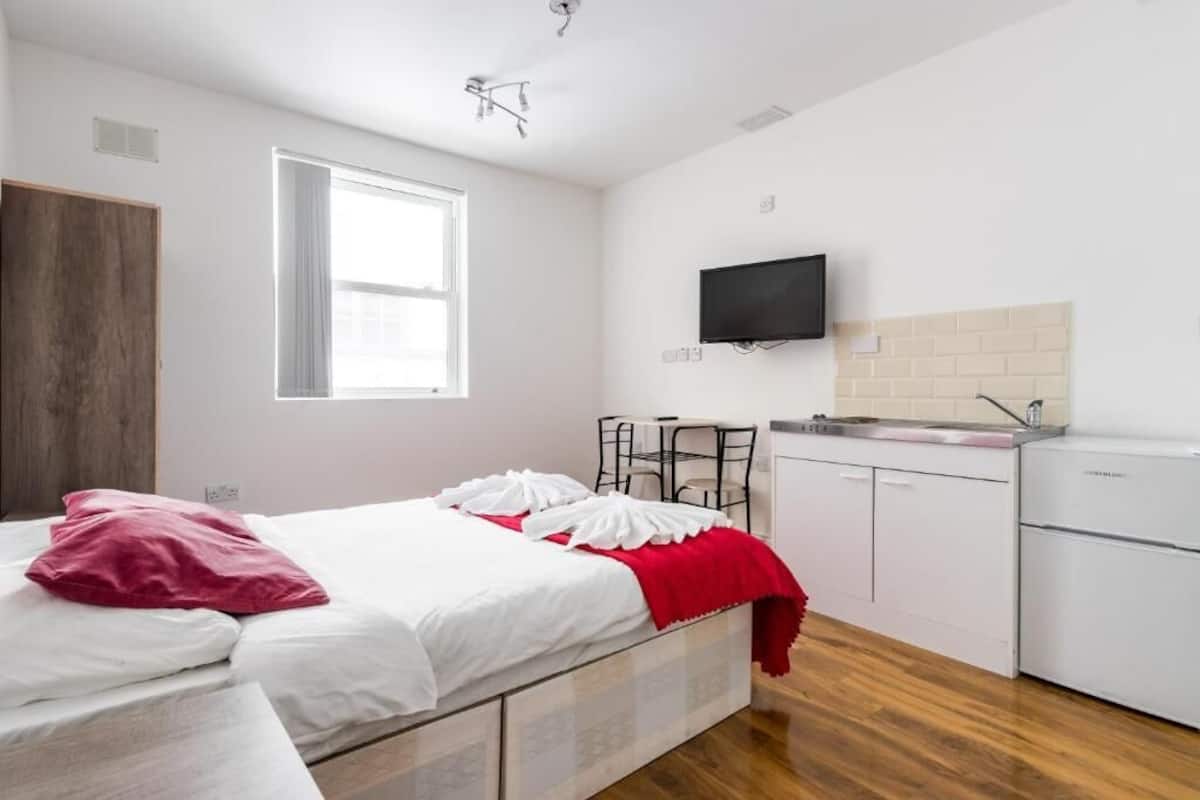 Un dormitorio con cama, una mesita, televisor y kitchenette.