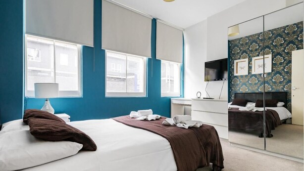 Una habitación de hotel moderna con una cama grande, un escritorio, un espejo y vistas a la ciudad a través de las ventanas.