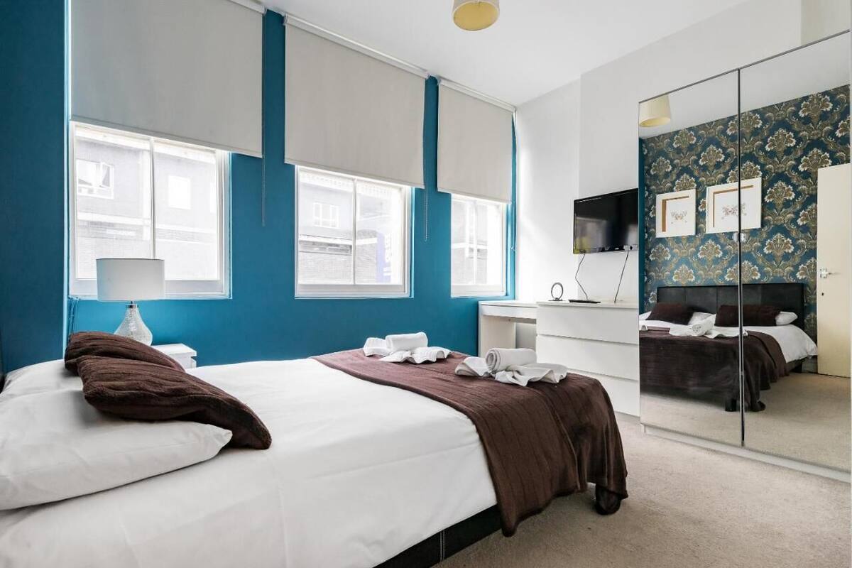 Una habitación de hotel moderna con una cama grande, un escritorio, un espejo y vistas a la ciudad a través de las ventanas.
