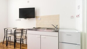 Una cocina compacta con un refrigerador blanco, un televisor negro montado en la pared y un pequeño comedor con dos sillas.