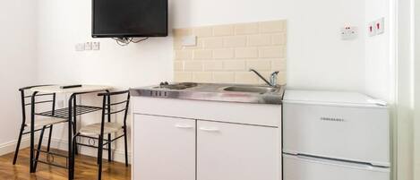 A compact kitchen with a white refrigerator, a black TV mounted on the wall, and a small dining area with two chairs.