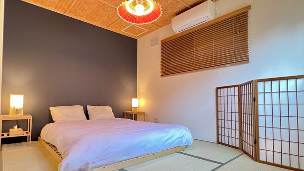 Une chambre d’hôtel avec un lit, des lampes de chevet, un climatiseur et un paravent japonais.