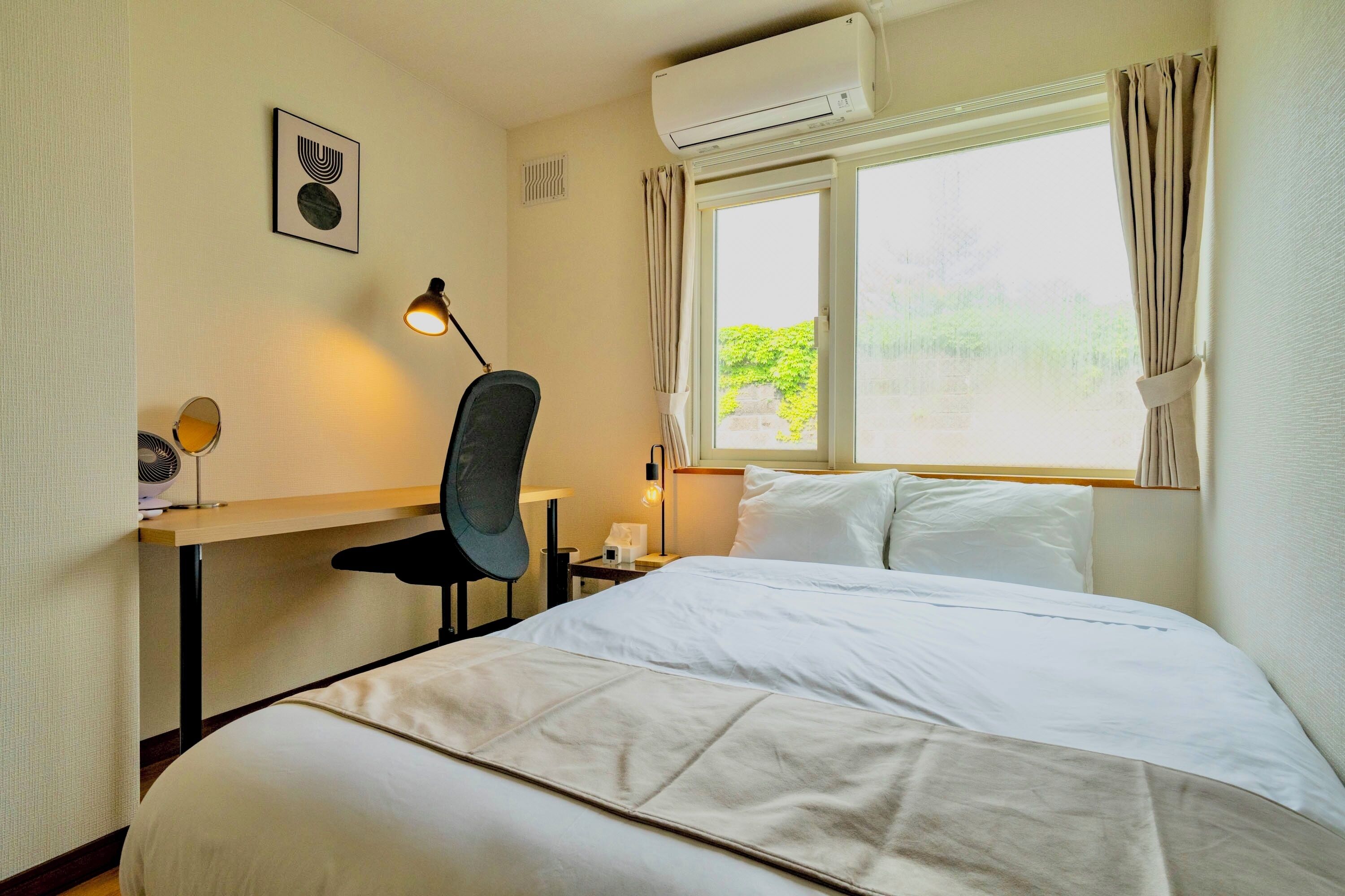 Een hotelkamer met een bed, bureau, stoel, lamp en raam met gordijnen.