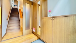 Un escalier en bois menant à un palier où se trouve un panneau d’indication concernant la sécurité incendie, une armoire en bois ornée d’un vase de fleurs et un tapis bleu au pied de l’escalier.