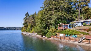 A lakeside cabin with a deck, chairs, and a wooden walkway along the water. - Captain s Retreat in Shelton (Shelton)