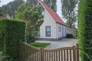Een tweelaags huis met een rood dak, een bakstenen gevel en een hekwerk voor de ingang.