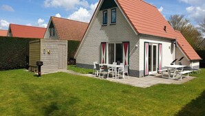 A two-story house with a red roof, a patio with a table and chairs, and a small shed in the backyard. - Modern Beach Retreat – Sauna (Breskens)