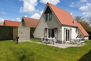 A two-story house with a red roof, a patio with a table and chairs, and a small shed in the backyard.
