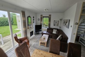 Een woonkamer met een bank, stoelen, een salontafel, een televisie en een open haard.