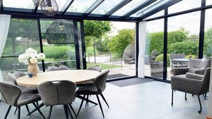 A conservatory with a round table and chairs, large windows, and outdoor seating. - Spacious Bungalow near Water (Breskens)
