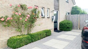A brick building with a paved driveway, a car parked on the right, and a wooden fence in the background. - Spacious Bungalow near Water (Breskens)