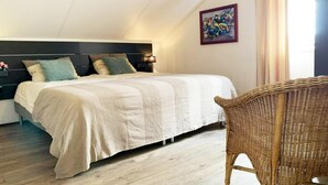 A bedroom with a bed, a headboard, a wicker chair, and a wall with a framed picture. - Spacious Bungalow near Water (Breskens)