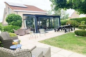 Une terrasse couverte, aménagée avec des meubles en osier, dotée d’une véranda et comprenant une table de pique-nique.