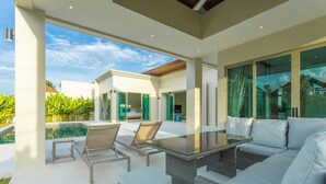 An outdoor patio with a glass table, wicker furniture, and a view of a swimming pool and house. - Brand New Completed Chalong A  v124 (Chalong)
