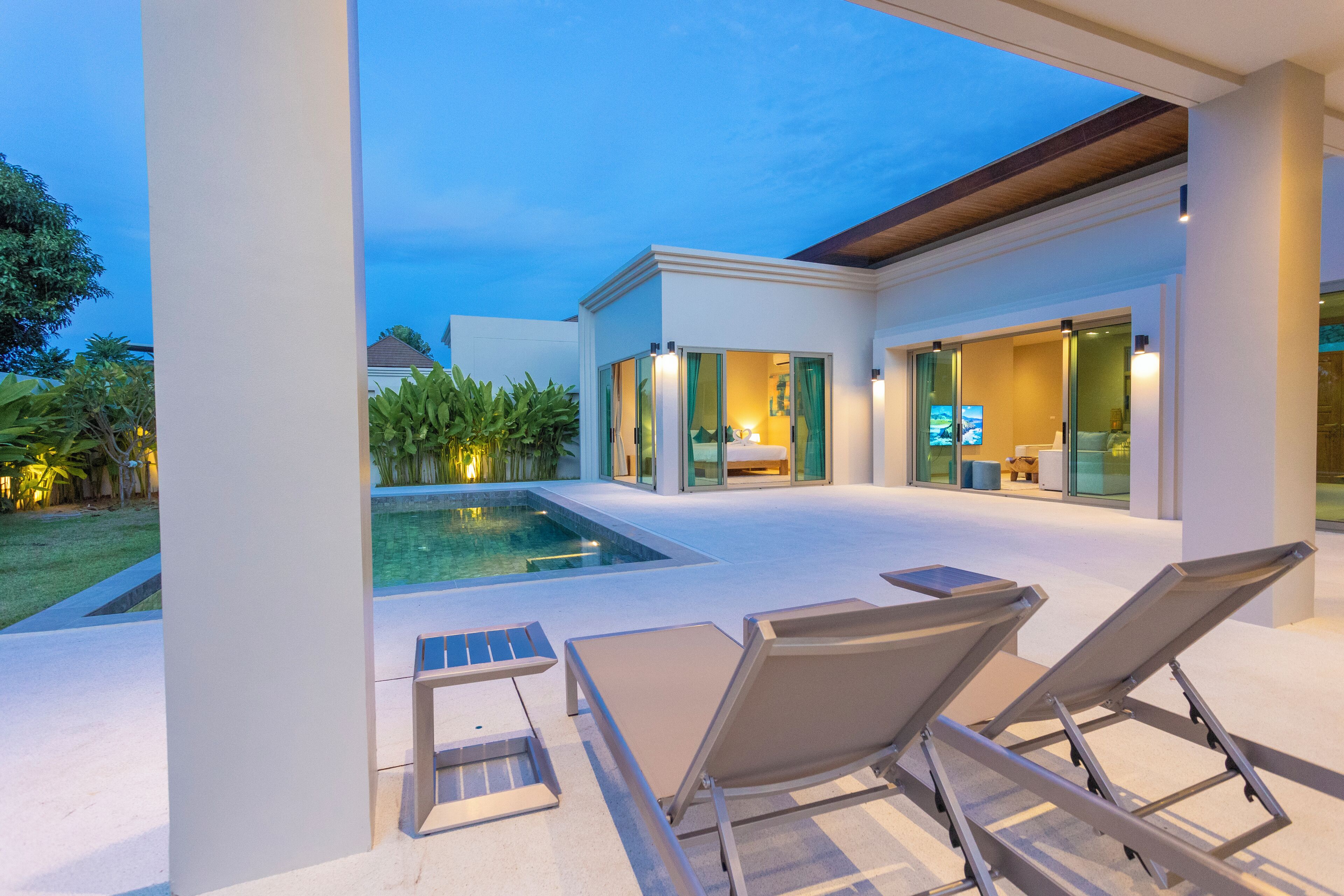 Un espace piscine extérieur moderne, doté de chaises longues, d’un petit bassin et d’un espace intérieur bien éclairé avec des portes vitrées.