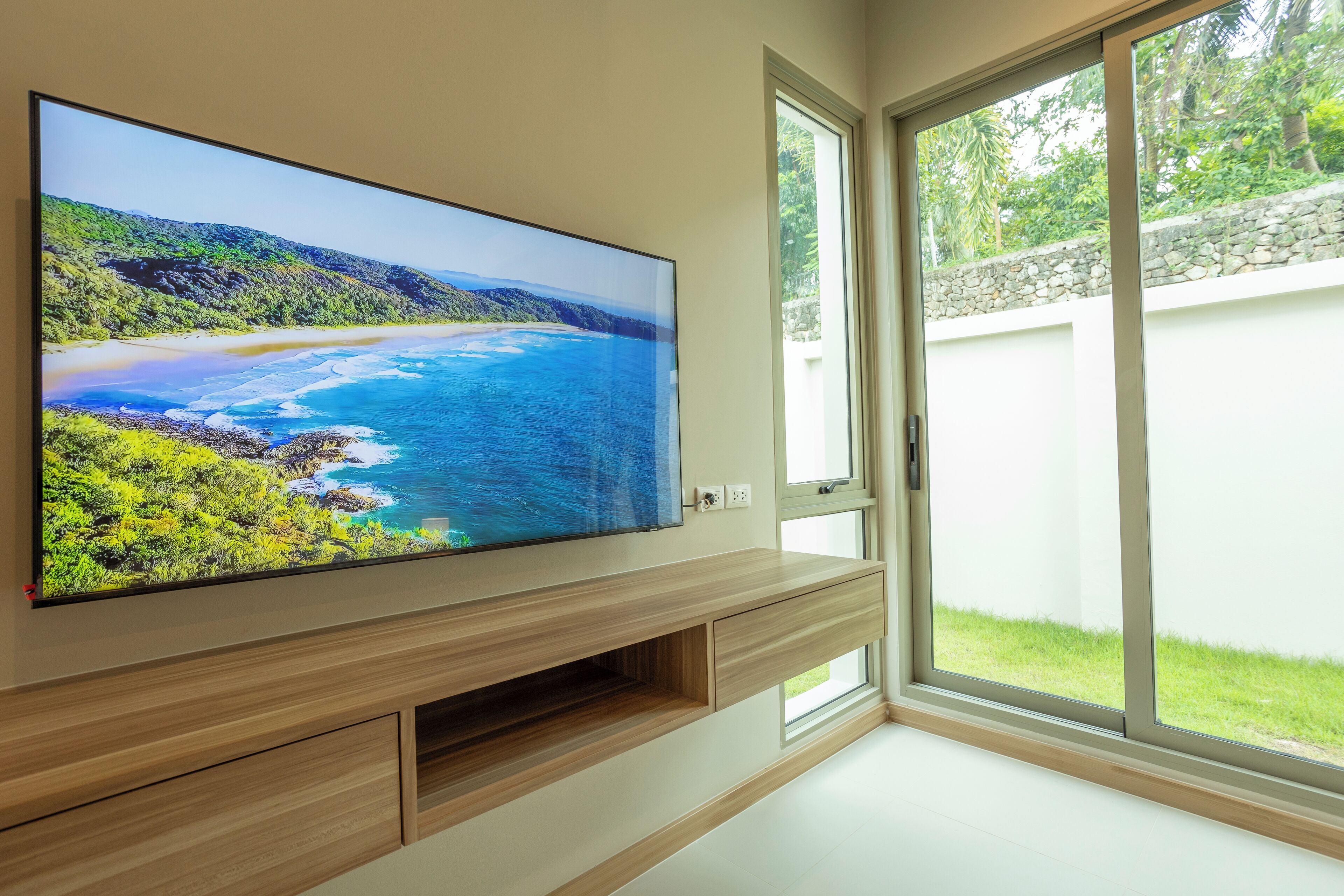 A flat-screen TV mounted on a wooden wall unit with a coastal landscape display.